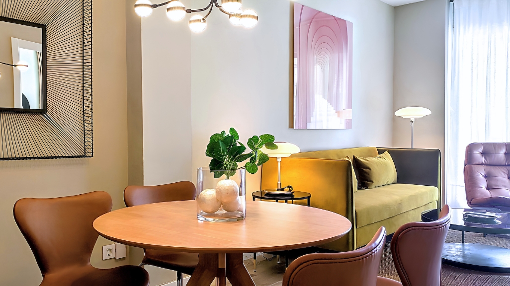 Living and dining area in a Bizflats serviced apartment in Barcelona, with round wooden dining table, leather chairs, olive green sofa, and artwork on the wall