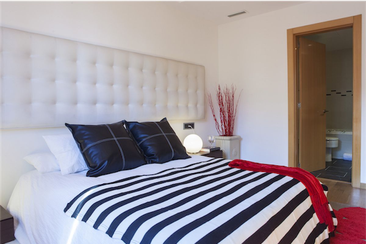 LaMimosa apartment for rent in Barcelona master bedroom with a large headboard covered in tufted white fabric 