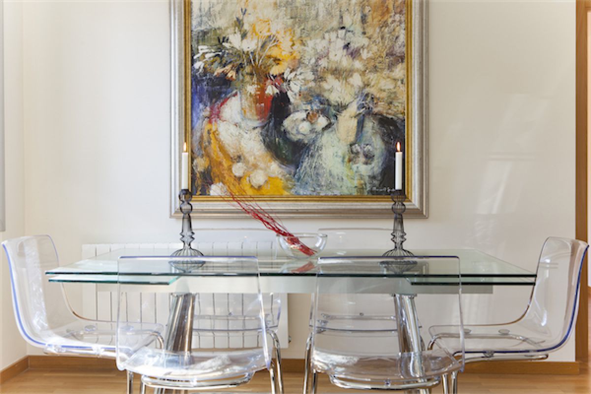 sleek dining area with a glass table, transparent chairs and original oil painting